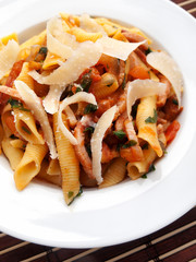 Italian penne pasta with bacon, tomatoes and parmesan shavings. Shot from above, close up