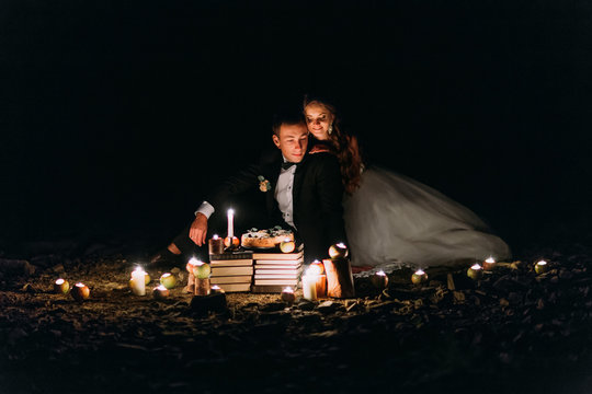 Loving Couple Share A Romantic Dinner With Candles And Cake  At Beach, Coast Against Wonderful Night