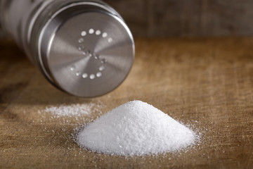 Fototapeta na wymiar Salt spilling on table from salt cellar