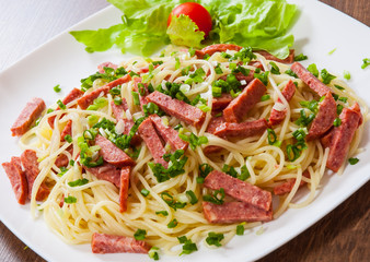 spaghetti pasta with salami sausage in a plate on wooden table
