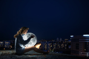 girl sitting on a roof at night, hugging the moon.