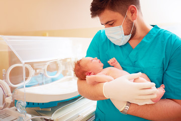 young adult man holding a newborn baby in hospital