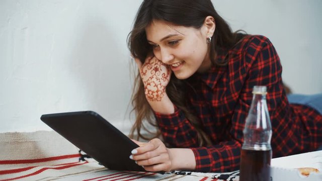 Asian woman eating pizza and looking at digital tablet computer at home