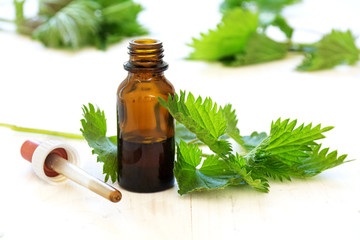 nettle tincture in a bottle and fresh leaves on white wood