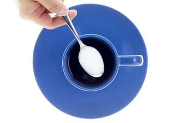 close-up shot of hand holding sugar in teaspoon over black coffee cup.