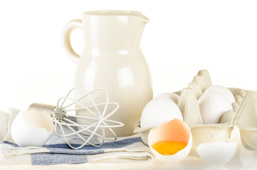 Baking ingredients and tools: eggs, flour, jug of milk, whisk an