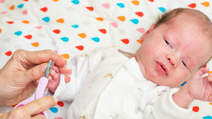 Mother cutting fingernails of her newborn baby daughter