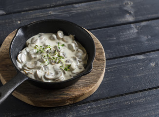 Creamy mushroom sauce in a pan on a wooden rustic board on a dark background