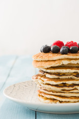Pancakes with blueberries and raspberry on blue wood background 
