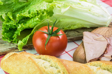 Ingredients for sandwich -tomatoes, lettuce, ham and french baguette.
