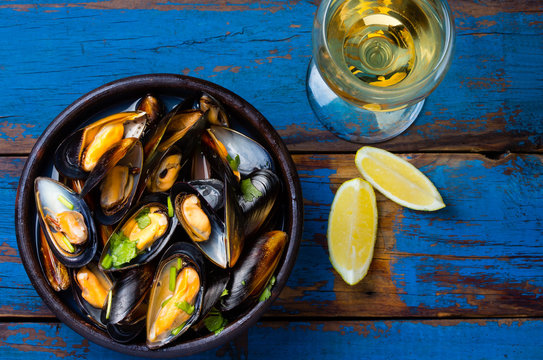 Mussels in clay bowl, glass of white wine and lemon