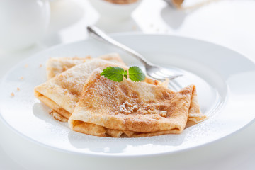 French crepes or pancakes with sugar powder, nuts and fresh mint on a white plate on a white background for breakfast, closeup