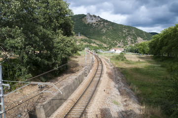 Obraz premium Iberian gauge railway track between Leon and Gijon on its way through La Pola de Gordon, Leon Province, Spain. In the background can be seen the town of Puente de Alba