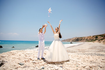 Fototapeta na wymiar Happy smiling bride and groom hands releasing white doves on a sunny day. Mediterranean Sea. Cyprus