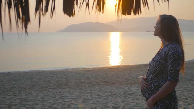 Prety millennial pregnant woman stroking belly and posing at sunset on the beach. Tropical vacation in Vietnam, 4k uhd 2160p
