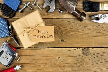 Fathers Day gift box with tag and corner border of tools and ties on a rustic wood background