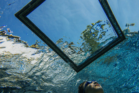 Teenage girl underwater, looking through frame on water surface