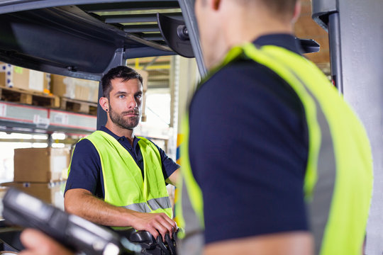Supervisor instructing forklift truck driver in distribution warehouse