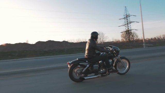 Young man riding motorcycle on the road at sunset, slow motion