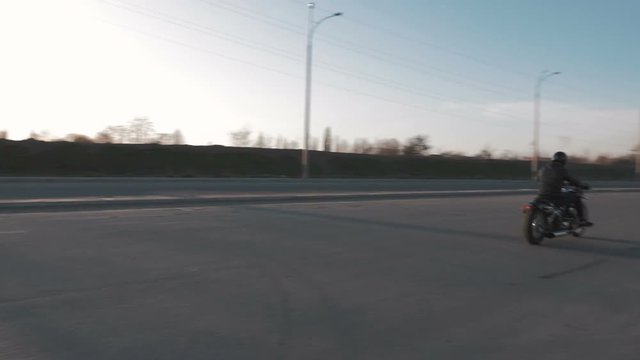 Young man riding motorcycle on the road at sunset, slow motion