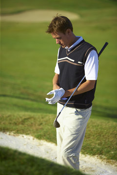 Golfer wearing golf glove carrying golf club under arm, looking down