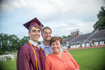 Young man standing with mother and father at graduation ceremony