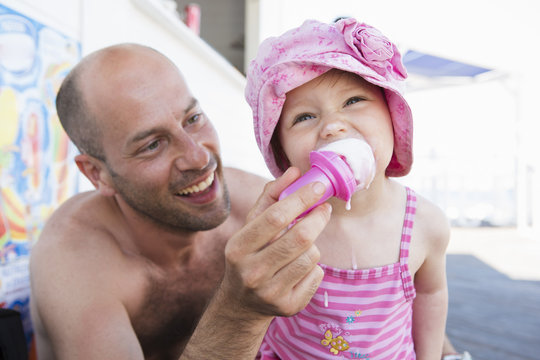 Father feeding toddler daughter ice cream cone on beach