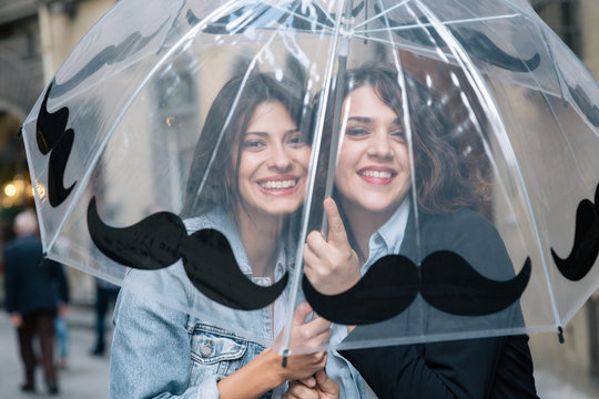 Lesbian couple underneath transparent umbrella looking at camera smiling, Florence, Tuscany, Italy