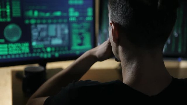 hacker works at computer with maps and data on display screens