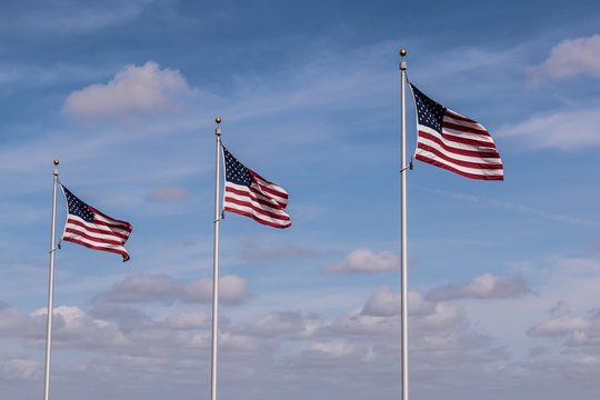 Row of three American Flags with a cloudy blue sky background.