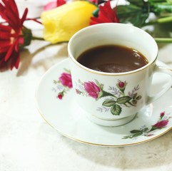 Coffee in floral tea cup with flowers in background, shallow depth of field
