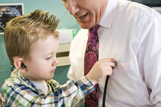 Male doctor letting young boy play with stethoscope in doctor's office