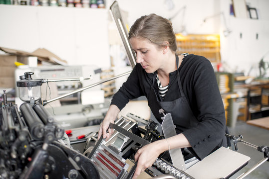 Female letterpress printer preparing print machine in workshop