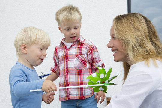 Mother and two young sons playing with pinwheel on patio