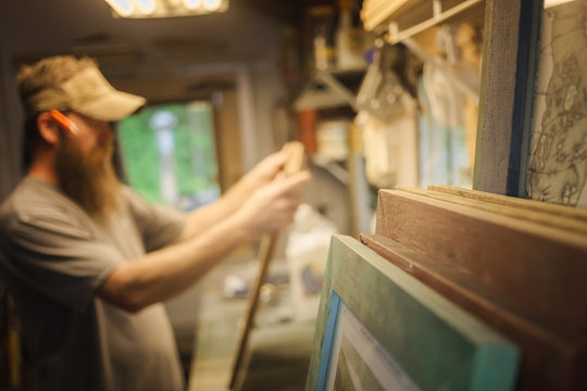 Artist working in workshop, wooden frames in foreground