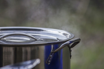 Steaming stainless steel pot outdoors with blurred background