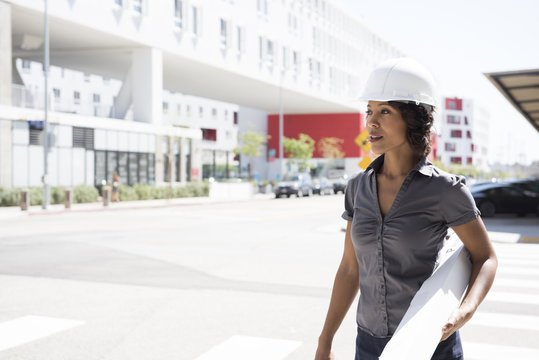 Young woman, wearing hard hat, carrying plans