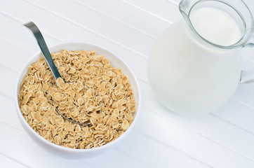 Healthy oatmeal in a white bowl and pitcher with milk
