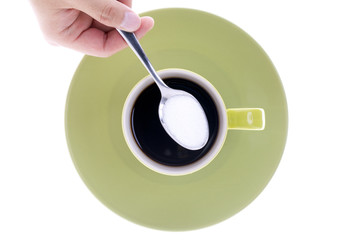 person holding a sugar spoon over green cup and saucer.