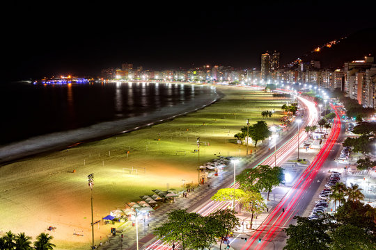 Aerial view of Capacabana Beach by night in Rio de Janeiro. The evening mist covers the shoreline, while cars leave long exposure light trails on Av. Atlantica