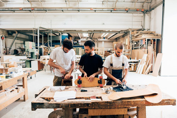 Front view of young men in carpentry workshop standing at workbench attaching wheels to skateboard