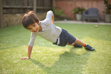 Boy doing one handed push up on grass looking at camera smiling