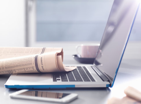 Reviewing financial affairs with newspaper market data page sitting on a laptop computer