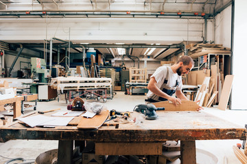 Young man in carpentry workshop looking down sanding skateboard