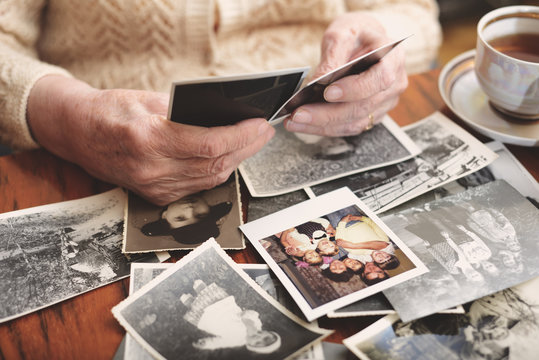Senior woman sitting at table, looking through old photographs, mid section