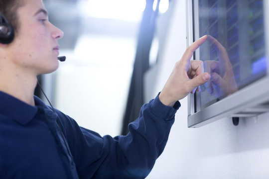 Low angle side view of young man wearing headset using touch screen computer monitor