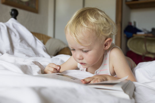 Female toddler lying in bed reading book