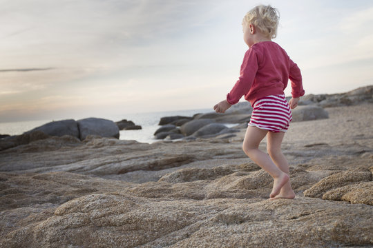 Female toddler toddling on coastal rock, Calvi, Corsica, France