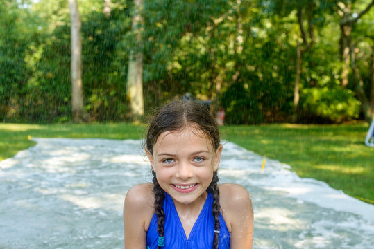 Portrait of girl in garden, slip n slide water mat behind her