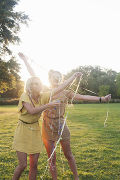 Two young women friends wrapping themselves in streamers at party in park